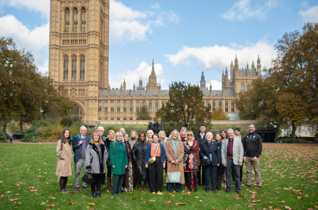 A group photo of everyone who road a coach down to London to attend the Gloucester Services 10th Celebration. They're posing in the park outside the Houses of Parliament.