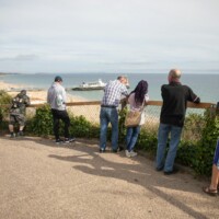 Group of participants photoed from behind standing along a fence, overlooking the beach and ocean.