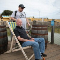 Gary sat on a folding beach chair and holding a golf club, as Kev stands behind him.