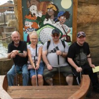 Four participants at an outdoor crazy golf place, sitting in a prop boat with golf clubs.