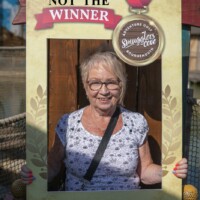 Helen, a participant, smiling and holding up a photo frame at an outdoor crazy golf place.