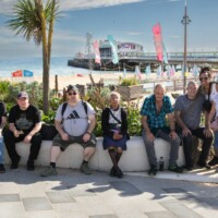 Group photo of participants sitting on a ledge in the sun, with the ocean and pier in the background.