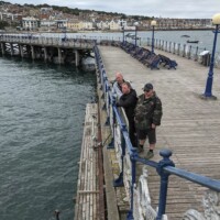 Gary, Jack, and Kev standing on a pier looking at the sea.