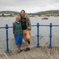 Two participants hugging as they lean against the railings, with the sea and boats in the background.