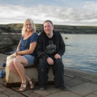 Rachel and Jack sat on a stone stand in front of the ocean.