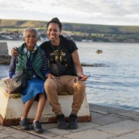 Two participants sitting down on a stone stand in front of the ocean.