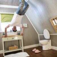 A participant posing in the 'Upside Down House'. He's pretending to be floating off, and holding onto the bathrooms vanity.