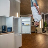 A participant posing in the 'Upside Down House'. He's standing on the ceiling, opening the fridge door.