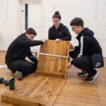 A group of 3 young people building a wooden planter. They're attaching a side panel to a longer panel.