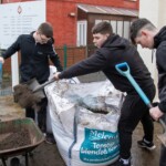 A group of 3 young people shovelling topsoil from a big bag to smaller wheelbarrows.