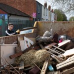 Young person chunking some wood into a skip outside St James City Farm.