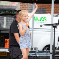 A young girl smiling and singing karaoke at the 2024 cultural fayre.